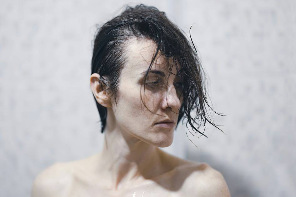 A close-up of silky, hydrated hair with a leave-in conditioner bottle on a natural background