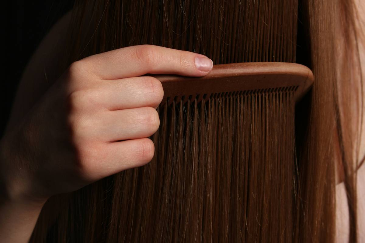 Woman using tangle release hair spray on wet curls while detangling with wide-tooth comb